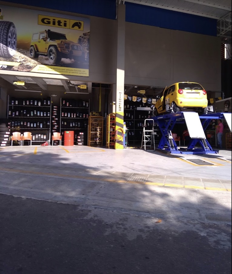Interior del taller con estantes de lubricantes, llantas y un carro en el elevador